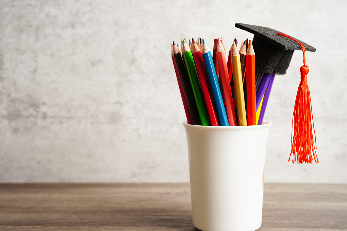 A cup holding colorful pencils with a graduation cap on top.